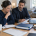 Two adults review documents together at a table beside an open laptop, notebooks and folders