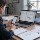 Woman reviewing messages on a smartphone and laptop at a desk with documents